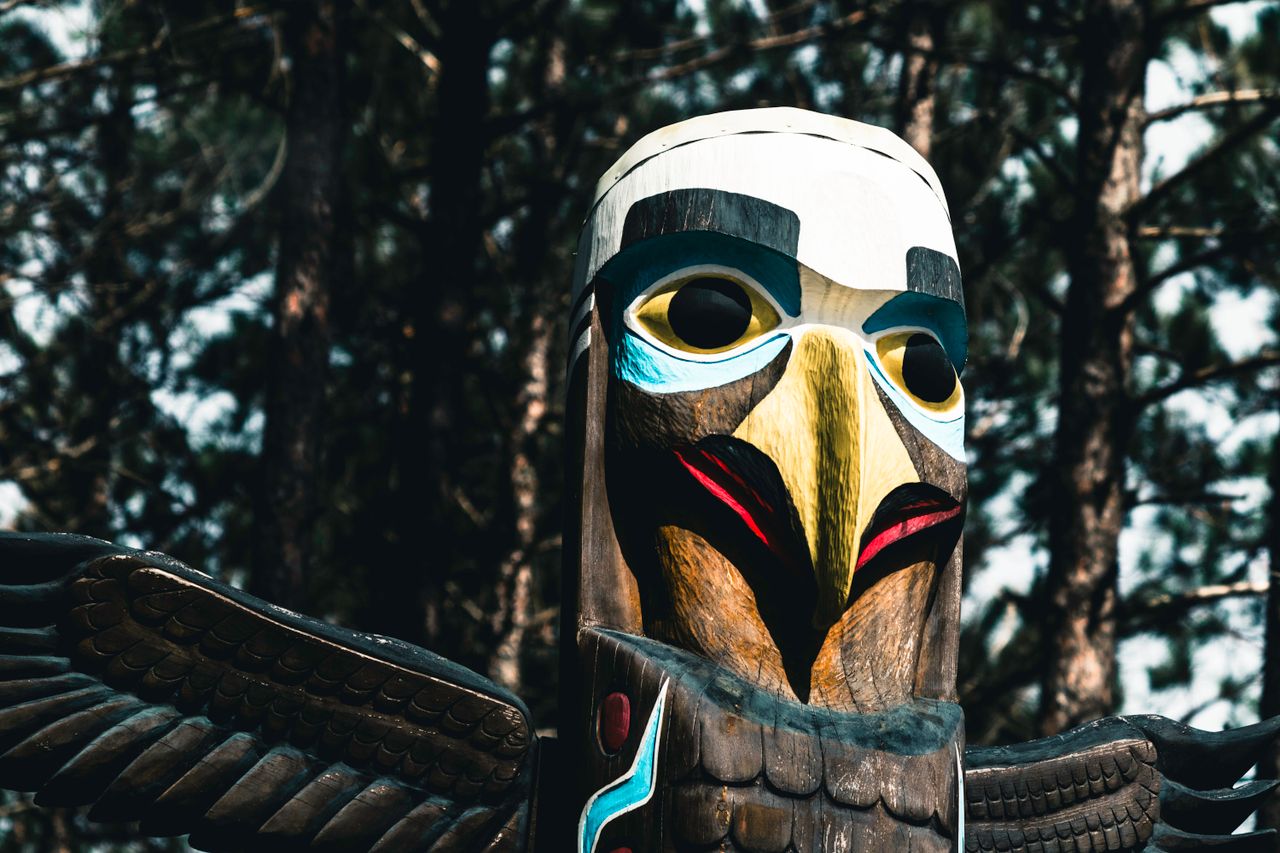 Close-up of a colorful totem pole in Algonquin Park, showcasing native art in a forest setting.