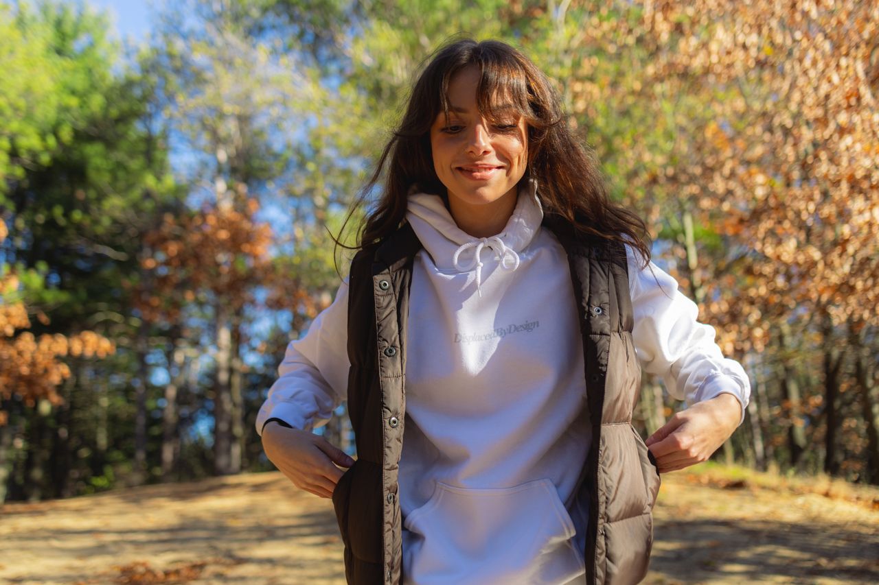 Happy woman wearing a white hoodie and vest in a sunny fall forest setting.